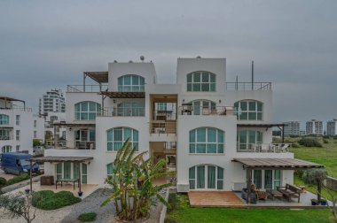 Kıyı dairelerinde kendine özgü bir tasarım ve deniz kenarında bulutlu bir gökyüzü altında yemyeşil bir manzara sergileniyor..