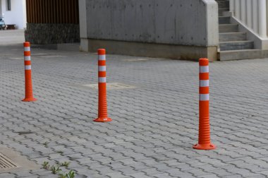Modern bir şehir manzarasında, üç parlak turuncu trafik konisi kaldırımlı bir yolda belirgin bir şekilde duruyor, yayalar için güvenli bir yol gösteriyorlar ve gün ışığında genel güvenliği artırıyorlar..