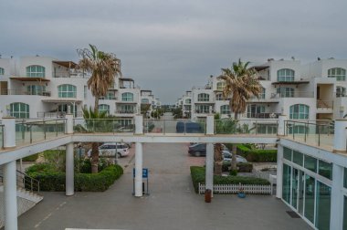 Palmiye ağaçları tarafından çerçevelenmiş şık beyaz binalar bulutlu bir günde barışçıl ve davetkar bir atmosfer yaratıyor..