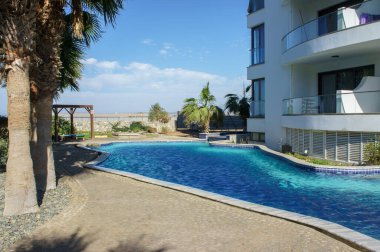 Sakin bir havuz, parlak bir gökyüzünün altında sallanan palmiye ağaçları tarafından çerçevelenmiş, gösterişli bir sahil villasına rahatlamaya davet eder..