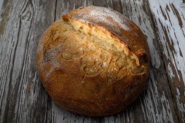 Sıcak, kabuklu bir ekmek somunu yıpranmış ahşap bir yüzeyde oturur ve doyurucu bir yemeğe davet eder..