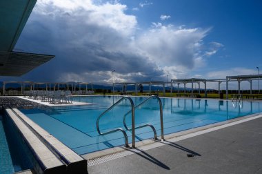 Sakin havuz başı kaçışı güneş ışığı altında parlarken fırtına bulutları beliriyor, öğleden sonra dinlenmeye ve sükunete davetiye çıkarıyor..