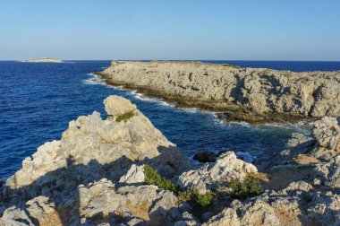 Engebeli kayalıklar parlak mavi denizi kucaklıyor. Güneş ufukta yavaşça batarken büyüleyici bir manzara yaratıyor..