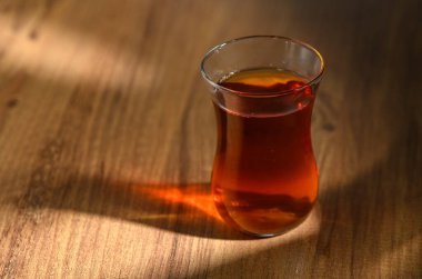 Sıcak, güzel kokulu çayla dolu bir bardak, yumuşak öğleden sonra ışığıyla aydınlatılmış, ahşap bir masada oturur..
