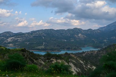 Yuvarlanan dağlar, gün batımında gökyüzünde süzülen bulutlar gibi parıldayan turkuaz bir göl oluşturur. Yamaçlar boyunca kır çiçekleri açar, doğanın başyapıtının huzur veren güzelliğini arttırır..