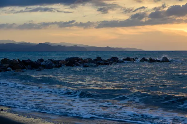 Sıcak altın güneş ışığı, gün batımında Kıbrıs 'ın kayalık kıyılarını aydınlatıyor. Sakin dalgalar, parlayan gökyüzü ve deniz kenarındaki sakin ada atmosferi..