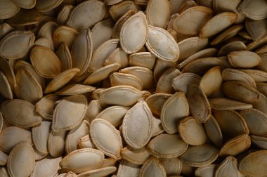 Dağılmış balkabağı tohumları sıcak sonbahar renklerini yansıtır. Sıcak bir mutfakta mevsimsel hasat hazırlıklarını ima eder. Her tohum doğanın cömertliğini ve yaratıcılığını temsil ediyor..