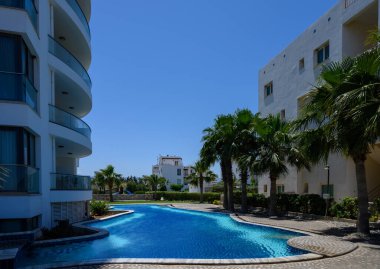 Kıbrıs 'ta güneşli bir sitede beyaz bir evin yanında açık yüzme havuzu.