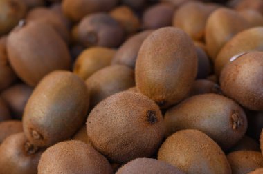 Olgun kivi meyvelerinden oluşan bir cömertlik marketin vitrinini dolduruyor. Sıcak güneşin altında tüylü dış görünüşleri parlıyor. Toprak renkler taze ürün arayanlar için cazip bir manzara yaratır..