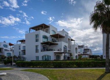 Terasları olan çarpıcı beyaz binalar yemyeşil çimenler ve palmiye ağaçları arasında oturur ve mükemmel bir sahil atmosferini kucaklarlar..