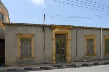 Tuhaf taş yapı, açık, güneşli bir gökyüzünün altında kırsal bir sokakla çevrili, karmaşık yeşil bir kapı ve kepenkli pencereler içeriyor. Nostalji ve tarihi çağrıştırıyor..