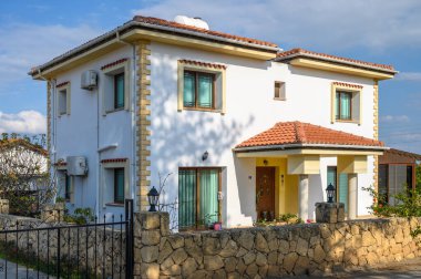 İki katlı güzel bir ev, çiçeklerle ve güneşli gökyüzüyle kucaklanan hoş bir giriş ile gururla ayakta duruyor..