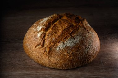Taze pişmiş zanaatkar ekmek somunu ahşap bir masada oturur ve kırsal dokusunu ve altın kahverengi kabuğunu sergiler..