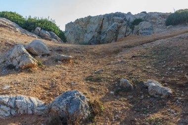 Altın güneş ışığı, kayalık bir araziye açılan dolambaçlı bir yolu aydınlatır. Keşifleri ve maceraları davet eder..