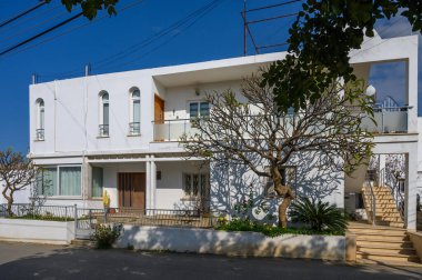 Sessiz bir caddenin yanında, gün ortası güneşinin sıcağında gururla duran büyüleyici beyaz bir bina..