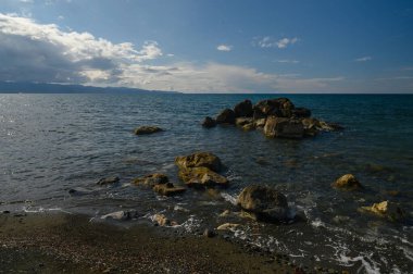 Dalgalar, su yüzeyindeki güneş ışığını yansıtan kayalık sahili ritmik olarak kucaklıyor. Görkemli bulutlar üzerimizde sürükleniyor, okyanus kenarında huzurlu ve ferahlatıcı bir atmosfer oluşturuyor..