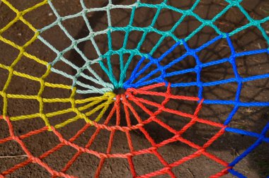 Parlak renkli ipler bir spiral ağ oluşturur. Gün ışığında dokulu bir zemine çarpıcı desenler gösterir..