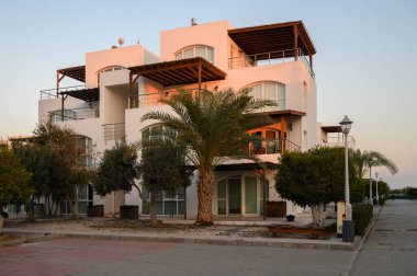 Modern mimari, sakin bir sahil manzarasında, alacakaranlıkta palmiye ağaçlarının arasında duruyor..