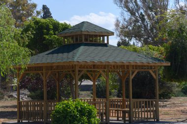 Bereketli yeşilliklerin ortasında, güzel işlenmiş ahşap bir çardak davetkar bir şekilde duruyor. Güneş ışığı ağaçların arasından süzülüp dinlenmek ve toplanmak için mükemmel bir dinlenme yeri oluşturuyor..