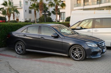 Gaziveren Kıbrıs Rum Kesimi -30.01.2025 Şık bir sedan palmiye ağaçlarının altına park edilmiş ve arka planda akşam saatlerinde çağdaş binalar bulunuyor.