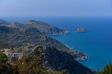 Görkemli uçurumlar, kıyı boyunca sakin bir sabahta canlı yeşillikler tarafından çerçevelenmiş ışıl ışıl mavi denizin üzerinde yükselir..