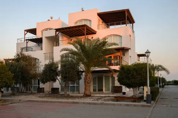 Modern mimari, sakin bir sahil manzarasında, alacakaranlıkta palmiye ağaçlarının arasında duruyor..