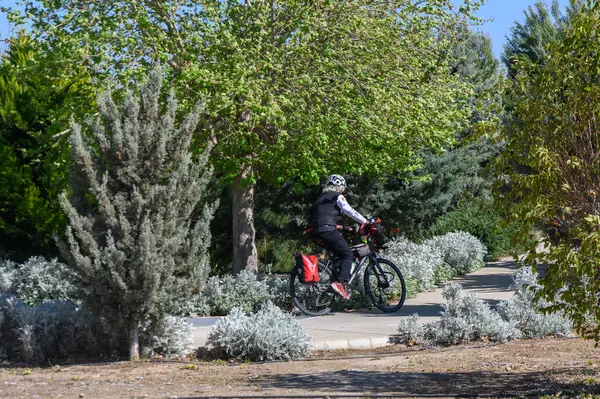 Bir bisikletçi, parlak mavi gökyüzünün altında yapraklı ağaçlar ve mis kokulu çalılarla çevrili dolambaçlı bir patika boyunca pedal çeviriyor. Doğa sesleri ve temiz havayla dolu canlı bir sabah..