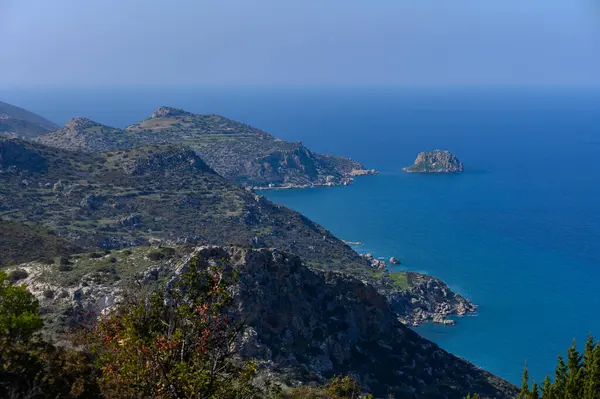 Görkemli uçurumlar, kıyı boyunca sakin bir sabahta canlı yeşillikler tarafından çerçevelenmiş ışıl ışıl mavi denizin üzerinde yükselir..