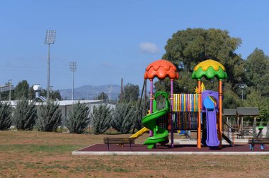 Parlak renkli slaytlar ve tırmanma yapıları çocukların geniş bir park ortamında keşfetmeleri ve eğlenmeleri için hazırlar. Yeşillik ve uzak dağlar dingin bir zemin oluşturur..