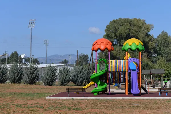 Parlak renkli slaytlar ve tırmanma yapıları çocukların geniş bir park ortamında keşfetmeleri ve eğlenmeleri için hazırlar. Yeşillik ve uzak dağlar dingin bir zemin oluşturur..