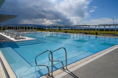 Parlak mavi sular güneşli havuzda güneşlenenleri bekliyor. Parlak gökyüzü ve uzak dağların altında..