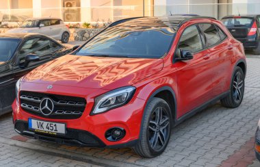 Gaziveren Kıbrıs Rum Kesimi -30.01.2025 Güneş öğleden sonra sıcacık gölgelerini sererken çağdaş bir otoparkta çarpıcı kırmızı bir SUV dinleniyor.