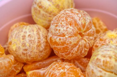 Olgun, soyulmuş narenciye meyveleri pembe bir kaseyi doldurur, parlak renklerini sergiler ve yumuşak ışıkta tazeliği davet ederler..