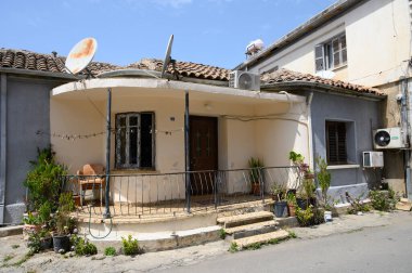 Küçük, davetkar bir ev, bitkilerle süslenmiş kıvrımlı bir verandayla gururla duruyor. Güneş ışığı dış tarafı yıkar, sıcak ve rahat hissettirir. Mahallede yaşam ve sükunet belirtileri var..