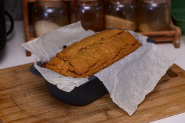 Sıcak bir muz ekmeği parşömene sarılı bir tavada dinlenirken, kavanozlar mutfak düzenine sıcak bir dokunuş ekliyor..