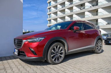 Gaziveren Kıbrıs Rum Kesimi - 15.02.2025 Çarpıcı kırmızı bir geçiş aracı, parlak güneş ışığı altındaki parlak modern binaların zeminine park etti.