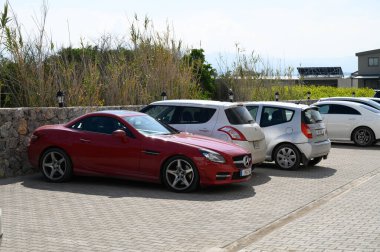 Gaziveren Kıbrıs Rum Kesimi 15.02.2025 Çarpışan kırmızı bir spor araba, güzel bir günün sıcak güneşinde güneşlenerek küçük arabaların arasına kurulmuştur..