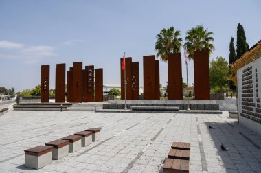 Modern bir meydanda sanat ve tasarımı yansıtan çelik heykeller dimdik dururlar. Sıcak öğle güneşinde palmiye ağaçları yavaşça sallanarak ziyaretçiler için sakin bir atmosfer yaratıyor..