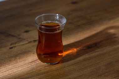 Kehribar çayıyla dolu narin bir bardak, öğleden sonra güneşiyle aydınlanan ahşap bir yüzeyde oturur..
