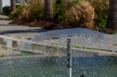 Bir çeşmeden fışkıran su, parlak güneş ışığı altında parlayan kristal berrak bir yüzme havuzunun yüzeyinde damlalar ve dalgalar oluşturur..