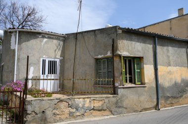 Sakin bir köyde solgun duvarları olan taştan bir ev duruyor. Canlı yeşil panjurlar yıpranmış dış ile tezat oluşturuyor. Çiçek açan çiçekler, sakin öğleden sonra güneşinde renk katar..