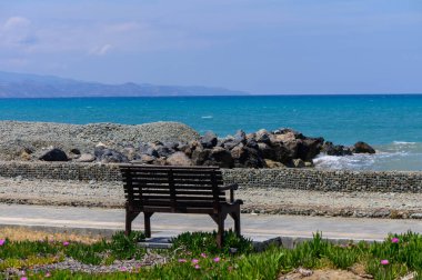 Kıbrıs adasında gün batımında denize bakan ahşap bir bank. Huzurlu manzara, sıcak Akdeniz renkleri, romantik atmosfer, rahatlamak ve doğanın tadını çıkarmak için mükemmel bir yer.