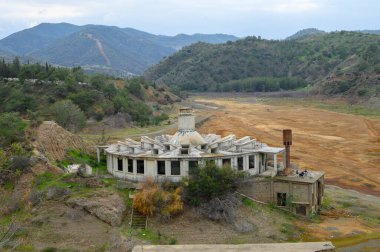 Çürüyen bina, bulutlu bir gökyüzünün altında yuvarlanan tepelerle çevrili çorak bir nehir kıyısında tek başına duruyor. Doğa bu unutulmuş yeri geri alır, bir entrika ve nostalji hissi uyandırır..