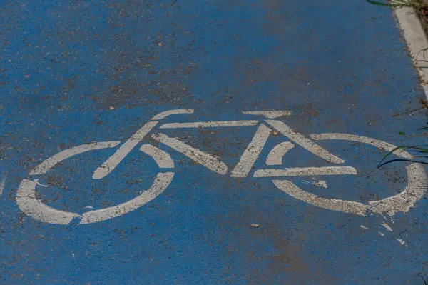 Taze, beyaz bir bisiklet sembolü parlak mavi bir yolda duruyor, bisikletçileri bu şehir ortamında bir yolculuğun tadını çıkarmaya davet ediyor. Güneş ışığı bölgeyi yıkıyor, neşeli atmosferi arttırıyor..