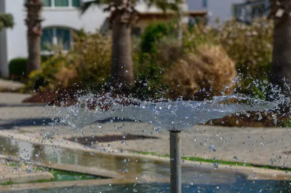 Çeşmeden havuza uçan su damlacıkları parlak güneş ışığının altında parlak yansımalar ve dalgalanmalar yaratır..