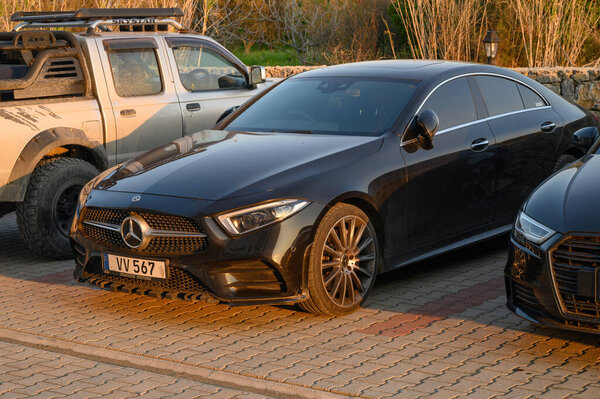Gaziveren Cyprus -30.01.2025 A sleek black sedan stands out among off-road vehicles under a warm sunset, showcasing elegance in a rustic setting.