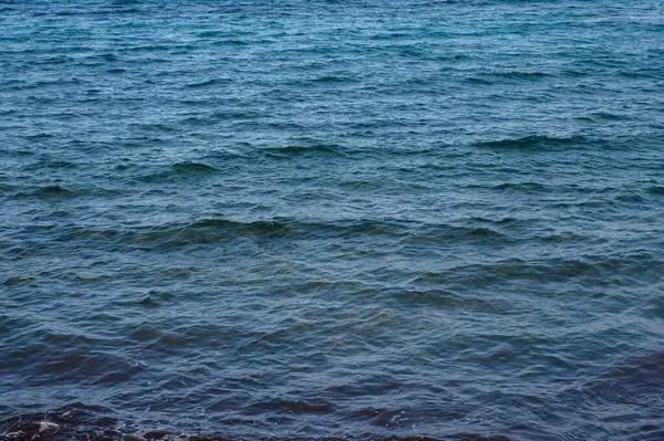 Sakin bir kıyı şeridindeki sakin suların üzerine güneş sıcacık bir parıltı saçarken, yumuşak dalgalar kıyıya vurur..