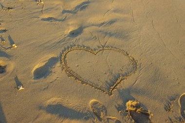 Gün batımının nazik kucaklamasında, kumlarda bir kalp şekli belirir, barışçıl dalgaların yanında aşkı sembolize eder.