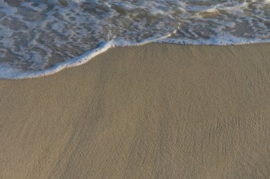 Güneş batarken yumuşak dalgalar sıcak kumu kucaklıyor ve huzurlu bir sahil atmosferi yaratıyor..