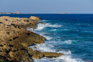Dalgalar kıyı şeridi boyunca engebeli kayalarla çarpışırken yumuşak dalgalar ritmik bir melodi yaratır..